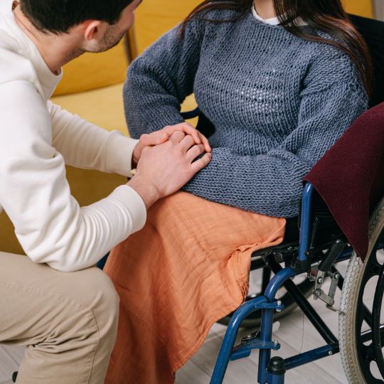 Une dame en chaise roulante qui tient les mains d'un homme